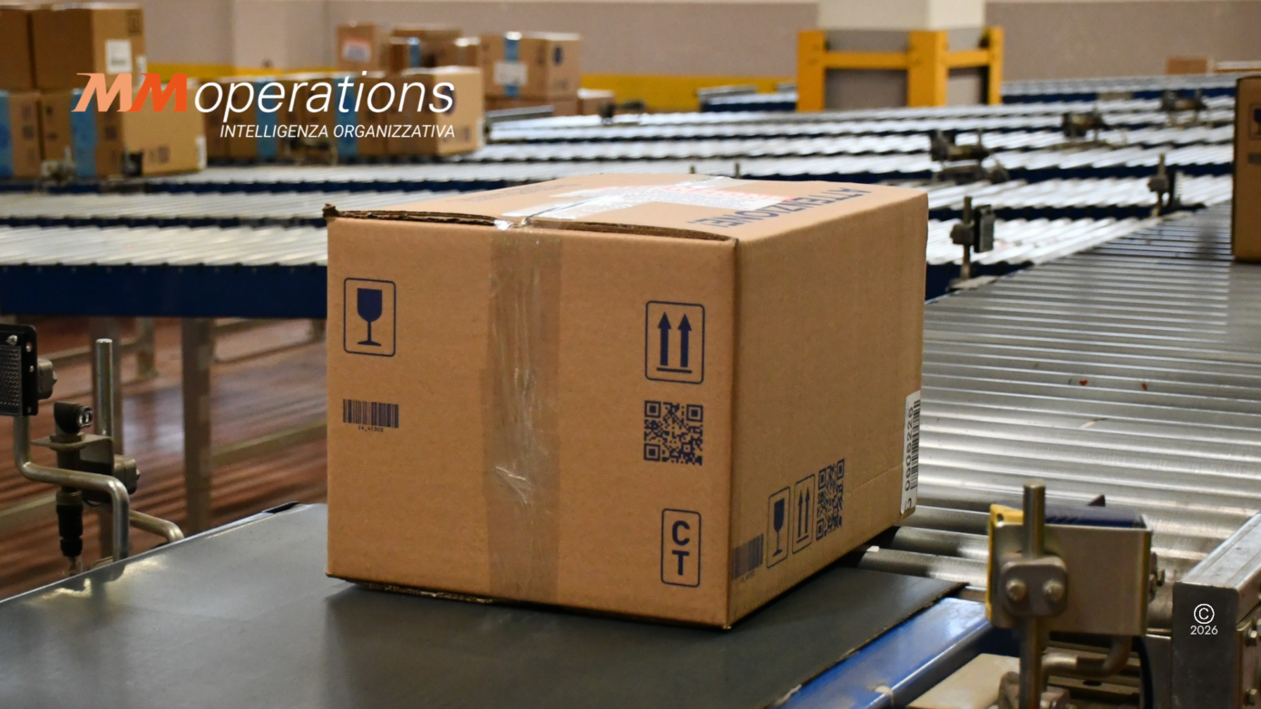 Collo in cartone con barcode, QR code e simboli di movimentazione su un nastro trasportatore a rulli in un magazzino MM Operations: identificazione del dato alla fonte per kpi logistici
